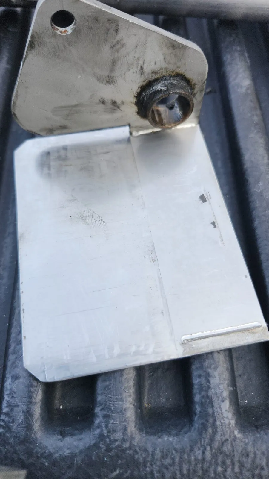A one-off aluminum mounting bracket with a bushing welded in, laid on a truck bed liner.