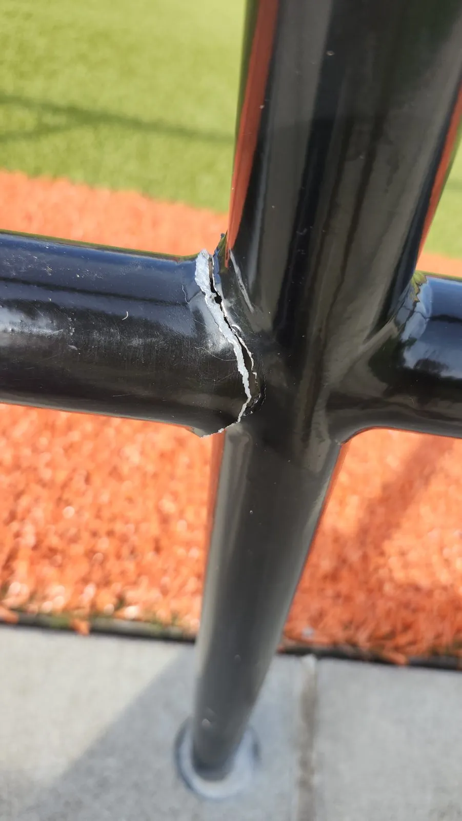A ballfield rail joint before repair, the post split open where the horizontal rail meets it.