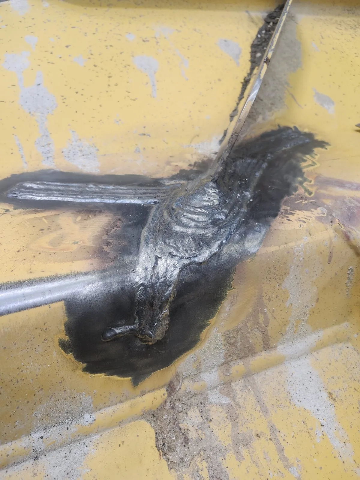 A crack on a yellow equipment bucket welded out, the weld ground and the surrounding paint burned back.