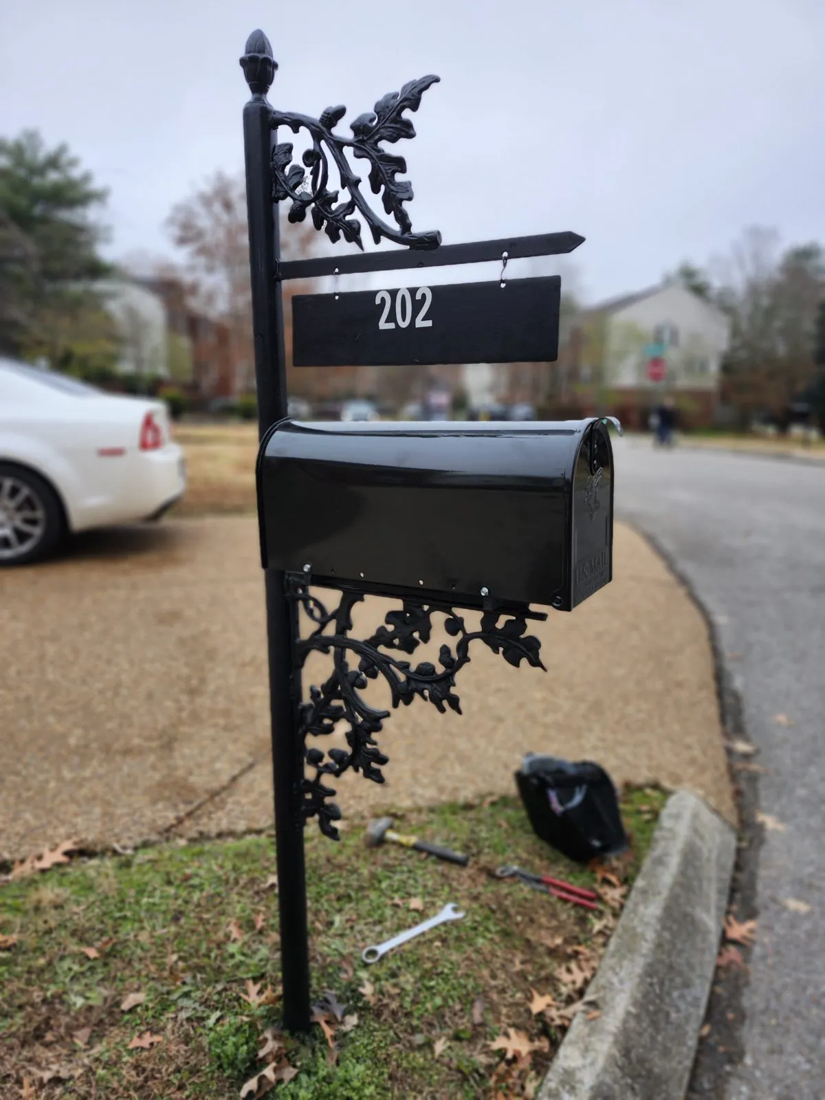 A black cast-iron mailbox post with oak-leaf scrollwork standing at a curb after repair.