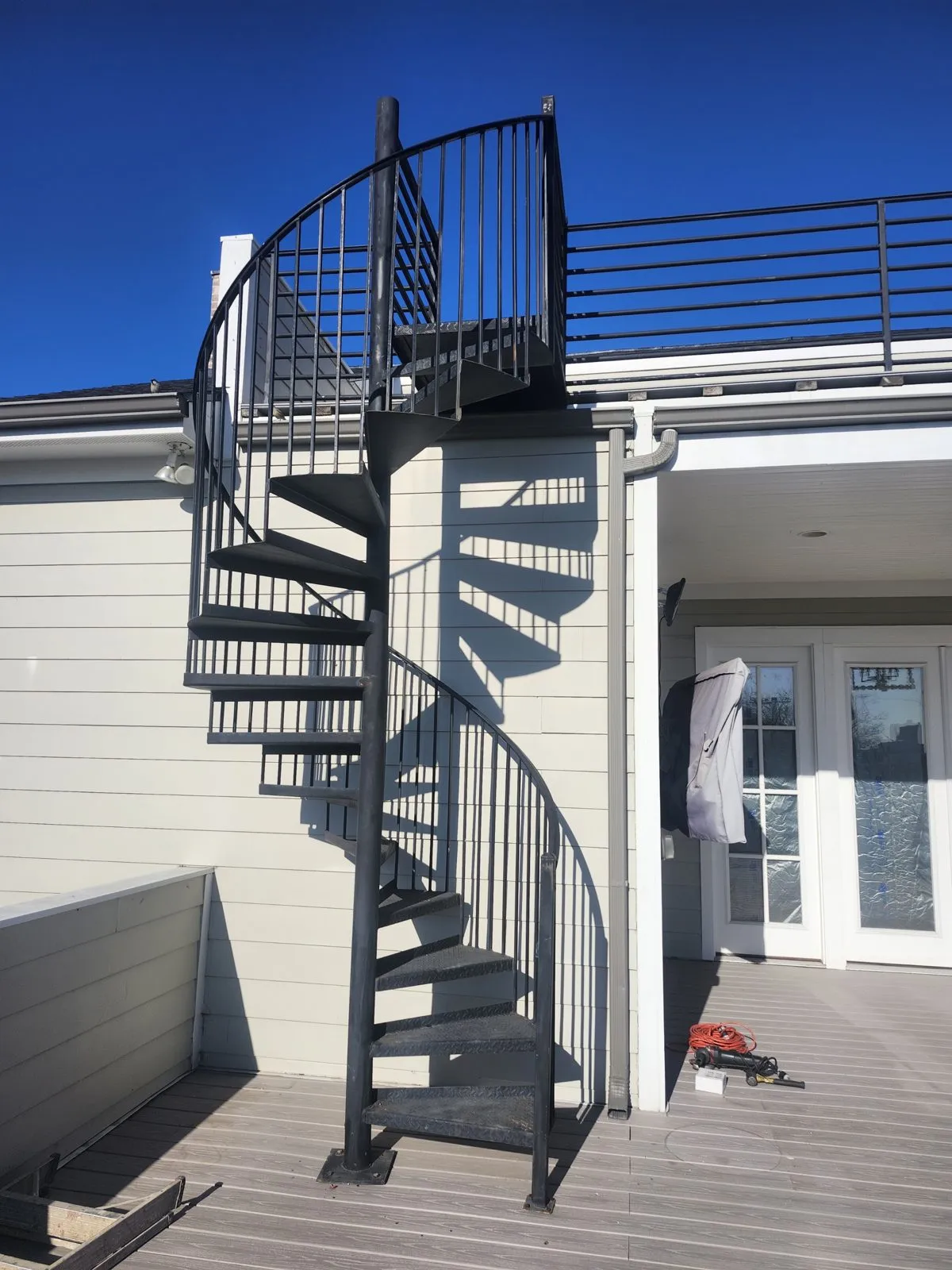 A black steel spiral staircase against the side of a house, landing on a composite deck.