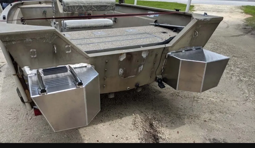 Aluminum flotation pods welded to both sides of a jon boat transom, the boat sitting on its trailer on a gravel lot.