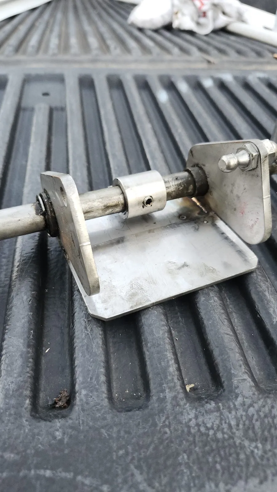 A stainless bracket repaired on site, resting on the bed liner of a pickup with the weld still visible.