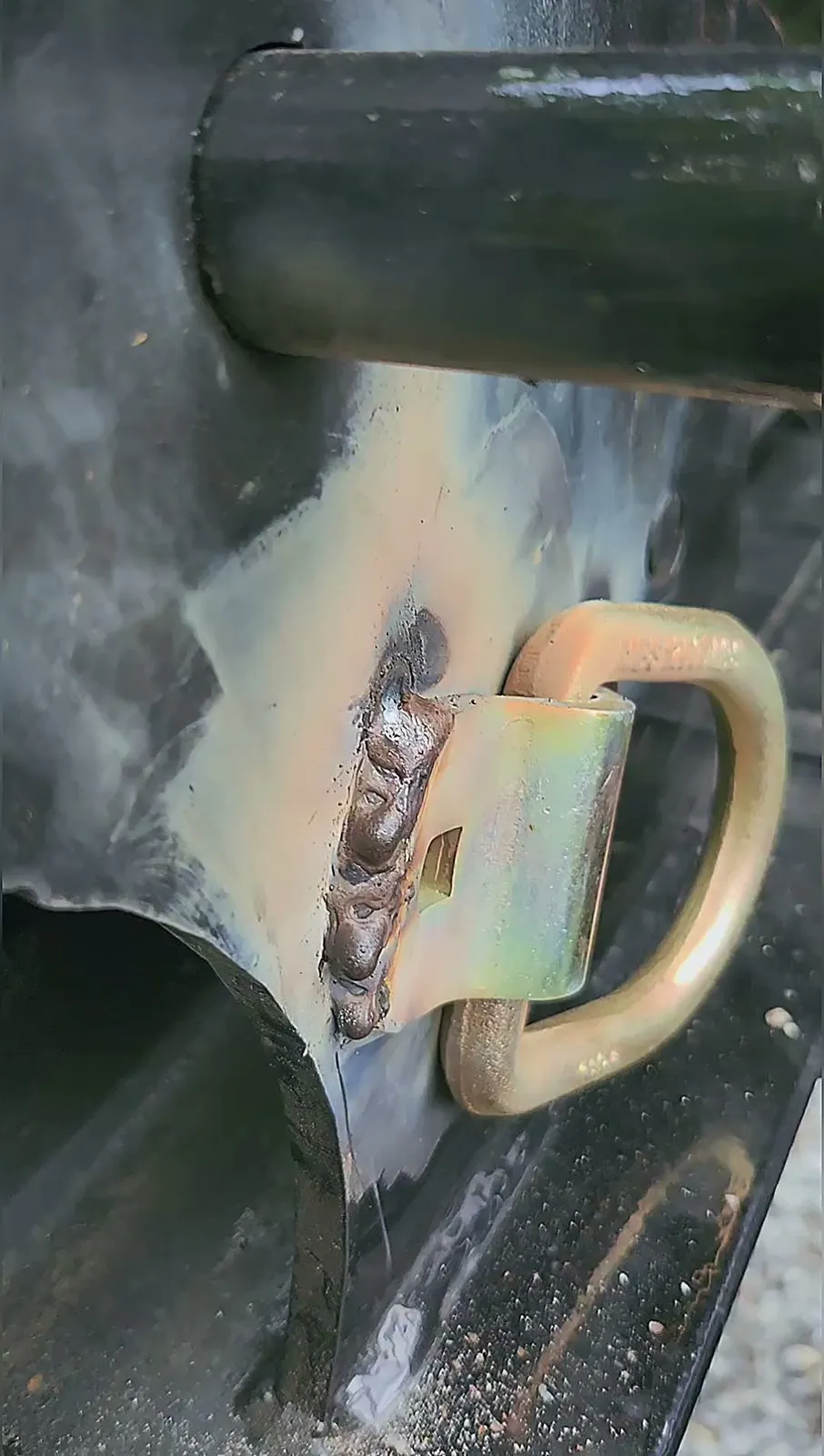 A new D-ring tie-down welded into the steel side rail of a trailer, the weld still bright.