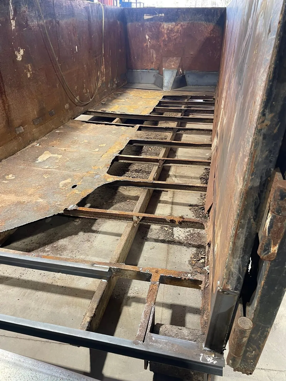 Inside the roll-off container with the failed floor cut out, the crossmembers exposed and the walls rusted.
