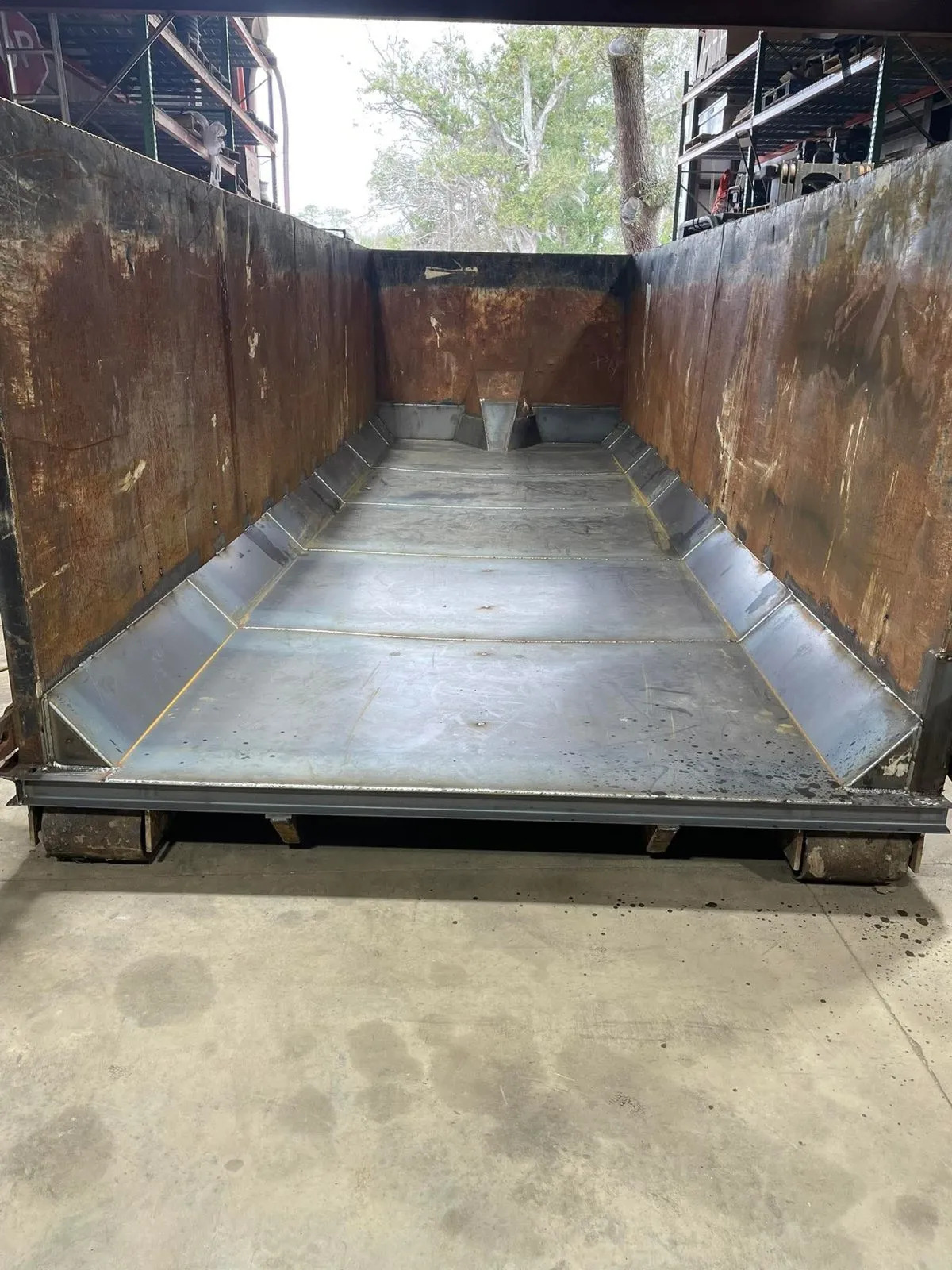 Looking into an open roll-off container with a fresh steel floor and side gussets welded in, the walls still showing their old rust.