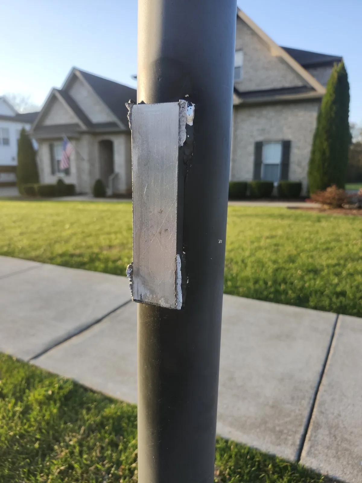 A steel post beside a sidewalk with a fresh patch plate welded over a rusted section, ready for paint.